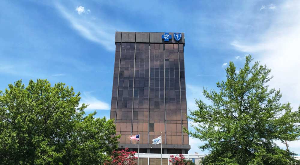 tall building with blue cross logo with blue sky and trees